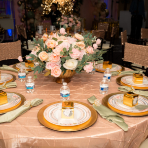 A stunning table setting featuring pink rose floral with blush pink table linen, complemented by a gold charger plate and matching silverware set.